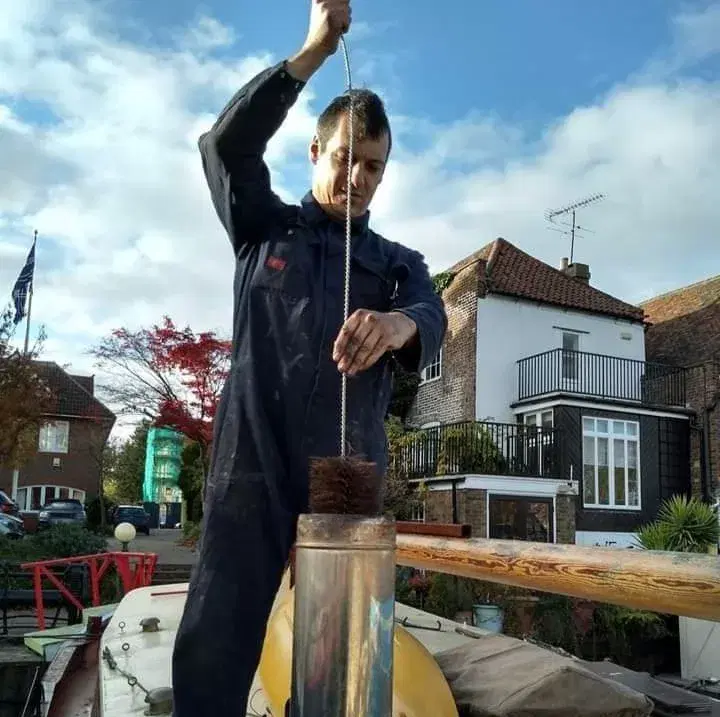 Marine heating engineer sweeping a narrowboat stove chimney flue to ensure safe operation and prevent Carbon Monoxide buildup.