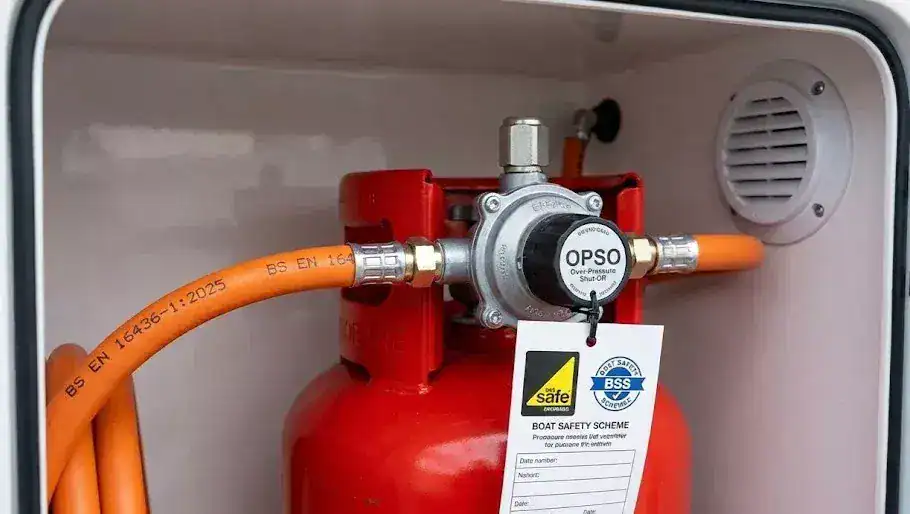 A modern marine LPG regulator with an OPSO safety device and a date-stamped BS EN 16436-1 high-pressure orange hose on a boat.