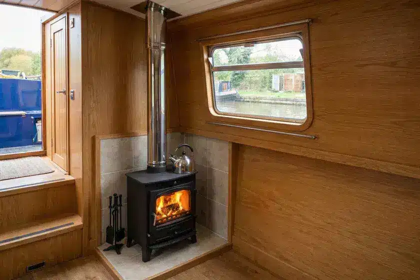 A professional boat stove installation featuring a stainless steel twin-wall insulated flue and a tiled fire-board hearth on a narrowboat.