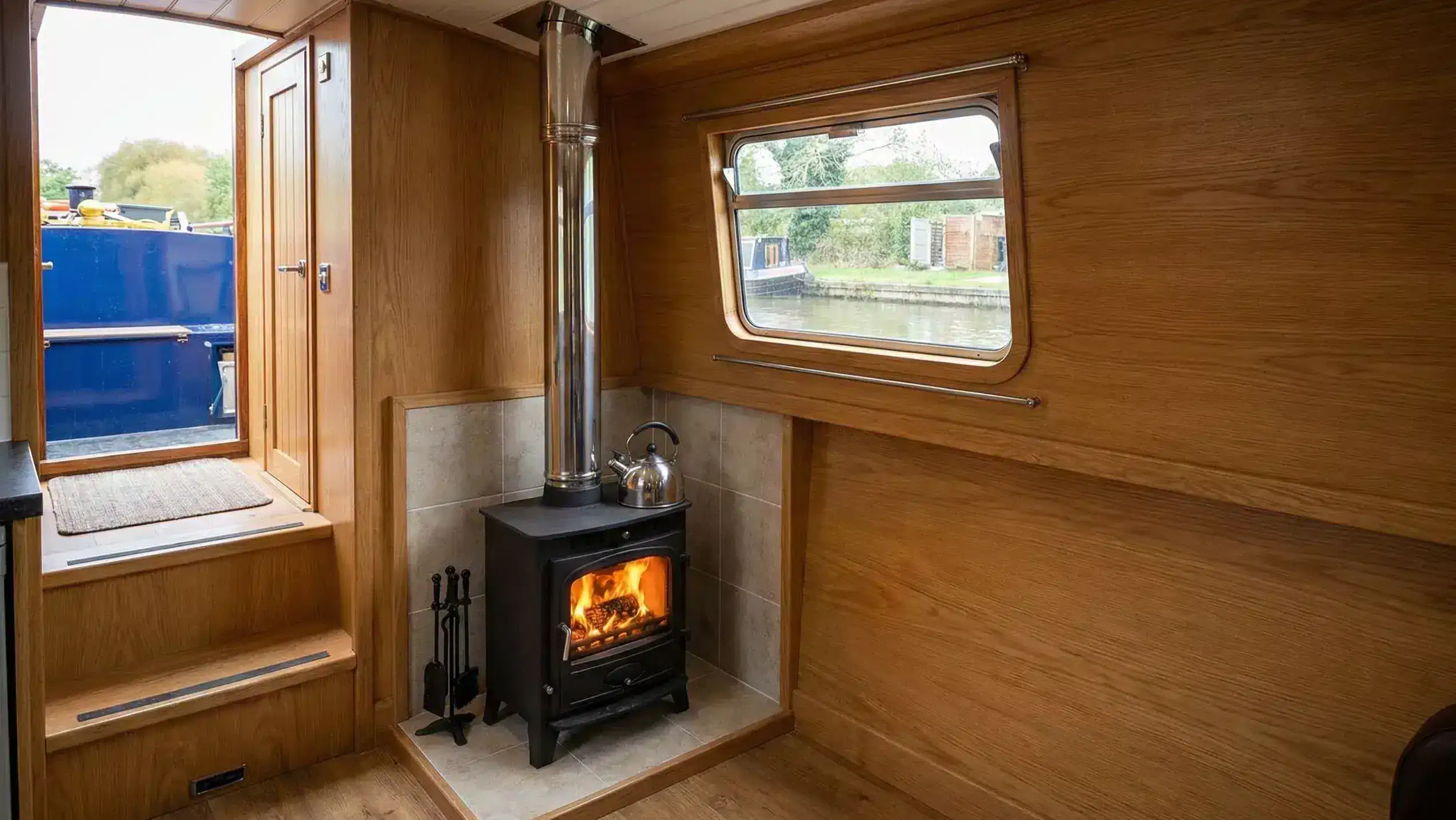 A professional boat stove installation featuring a stainless steel twin-wall insulated flue and a tiled fire-board hearth on a narrowboat.