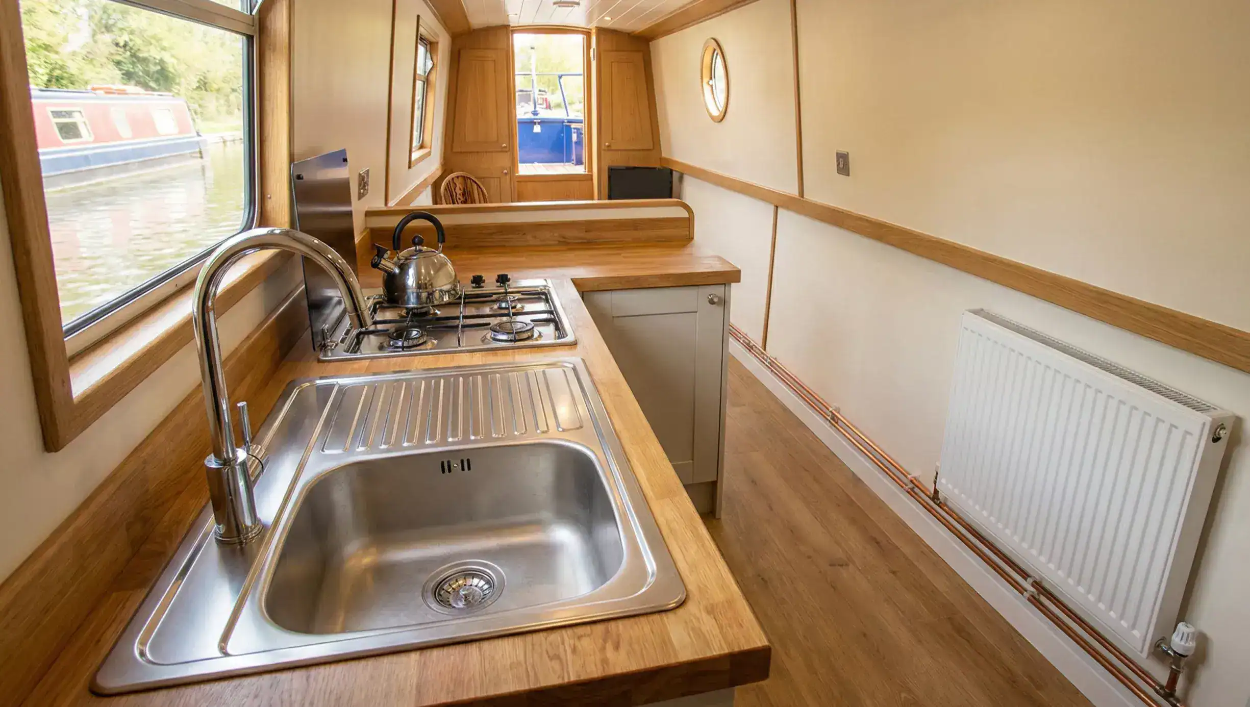 Modern narrowboat galley showing professional LPG gas hob installation, stainless steel plumbing, and a white central heating radiator