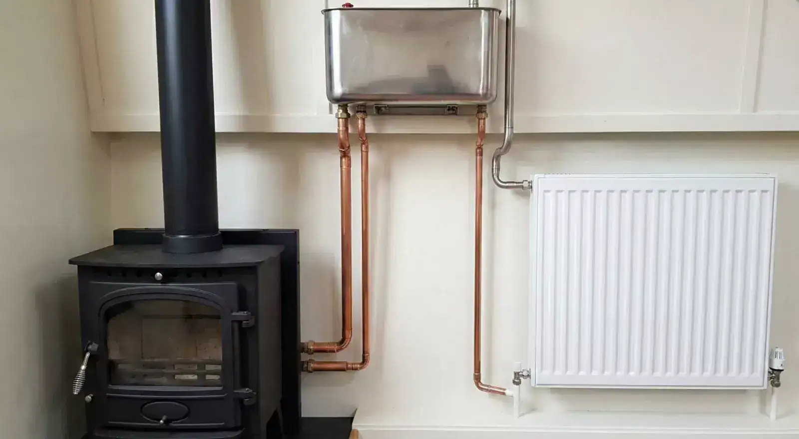 A professional marine back boiler installation featuring simple copper pipework leading to a radiator and a stainless steel open-vent header tank in a narrowboat.