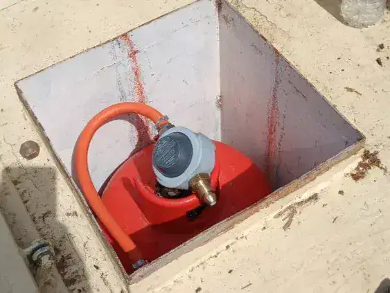 A modern marine LPG regulator with an OPSO (Over Pressure Shut Off) device connected to a red propane cylinder in a boat gas locker.