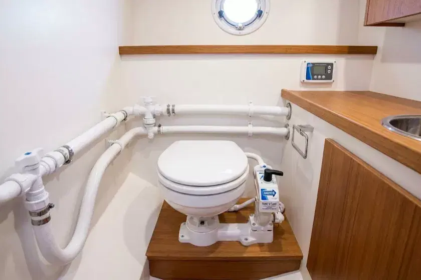 A professional photo of a Jabsco Twist 'n' Lock manual marine toilet installed in a clean boat head, showing secure sanitation-grade hoses and 304 stainless steel clips.