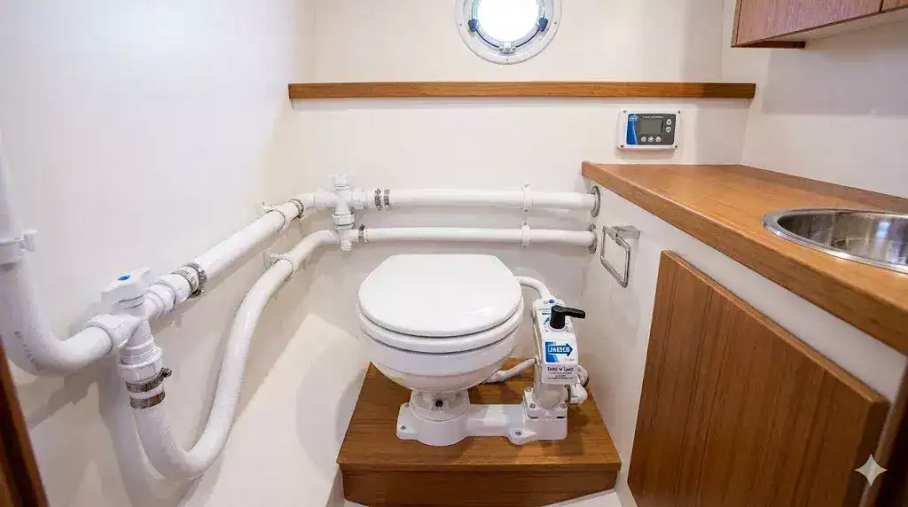 A professional photo of a Jabsco Twist 'n' Lock manual marine toilet installed in a clean boat head, showing secure sanitation-grade hoses and 304 stainless steel clips.