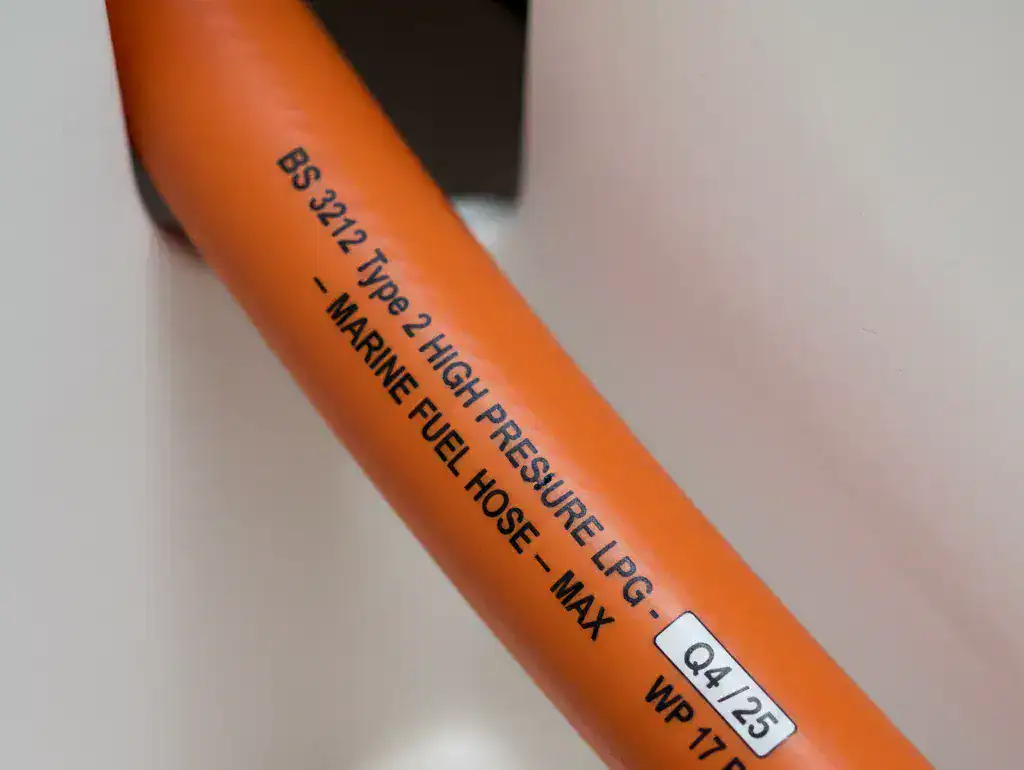 A detailed 4:3 close-up of high-pressure orange LPG hose markings showing the BS 3212 Type 2 certification and the manufacturer date stamp for safety compliance.