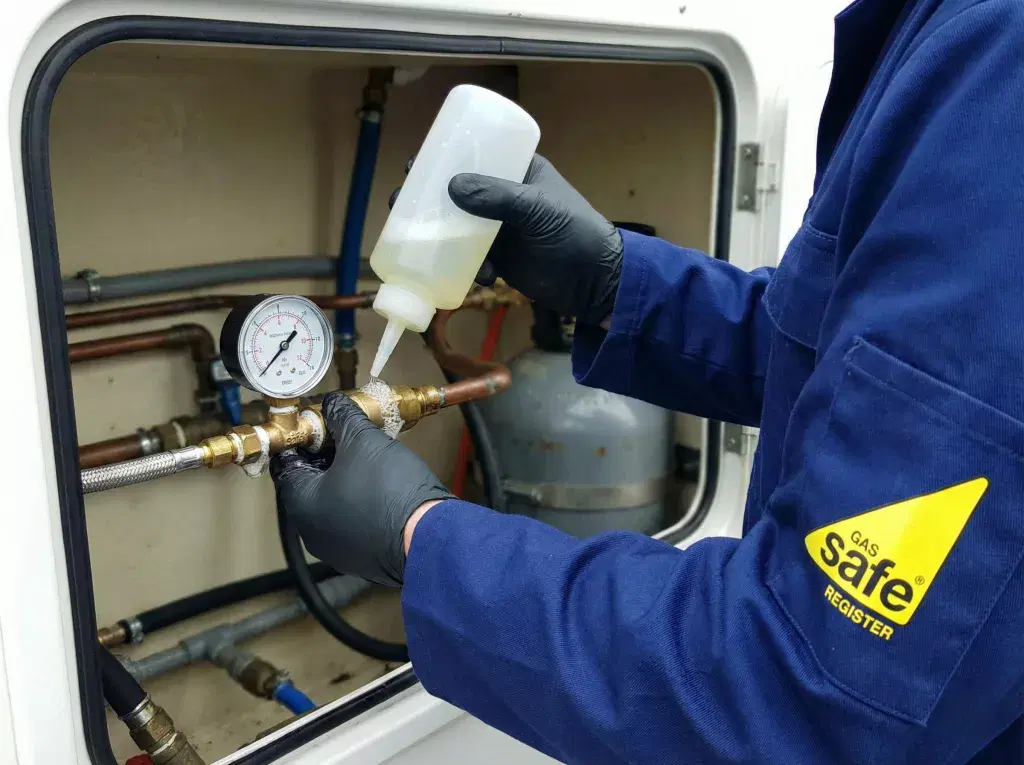 A technical shot of a Gas Safe registered engineer applying specialized leak detection fluid to a gas bottle gauge connection to check for bubbles and leaks.