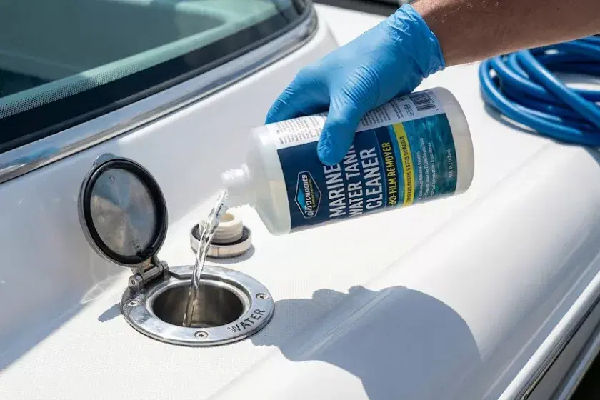 A photo of a boat owner wearing protective gloves while pouring a measured dose of non-chlorine water tank cleaner into a stainless steel deck-mounted freshwater fill point on a narrowboat.