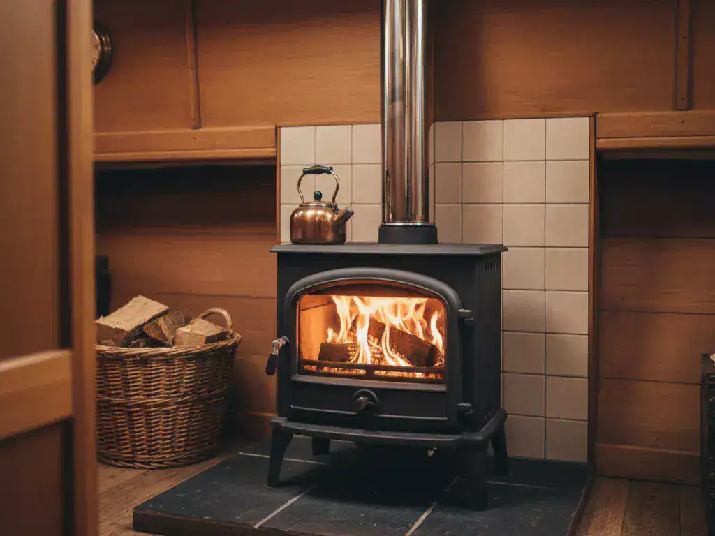 A cozy 4:3 view of a solid fuel stove with visible flames, featuring a properly installed twin-wall insulated flue and tiled hearth in a narrowboat.
