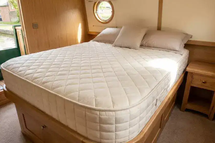 A high-resolution photo of a custom-shaped marine mattress perfectly fitted into a narrowboat island bed frame, featuring high-quality quilting and tailored corners in a modern cabin interior.