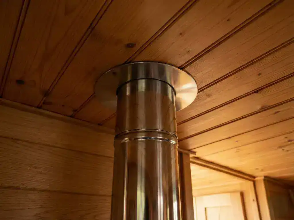 Close-up of a twin-wall insulated flue system passing through a narrowboat's timber-clad ceiling with a professional stainless steel finishing collar.