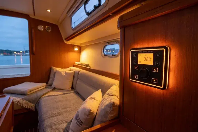 A cozy yacht saloon interior with a glowing digital diesel heater controller on the bulkhead, highlighting professional marine heating installation.