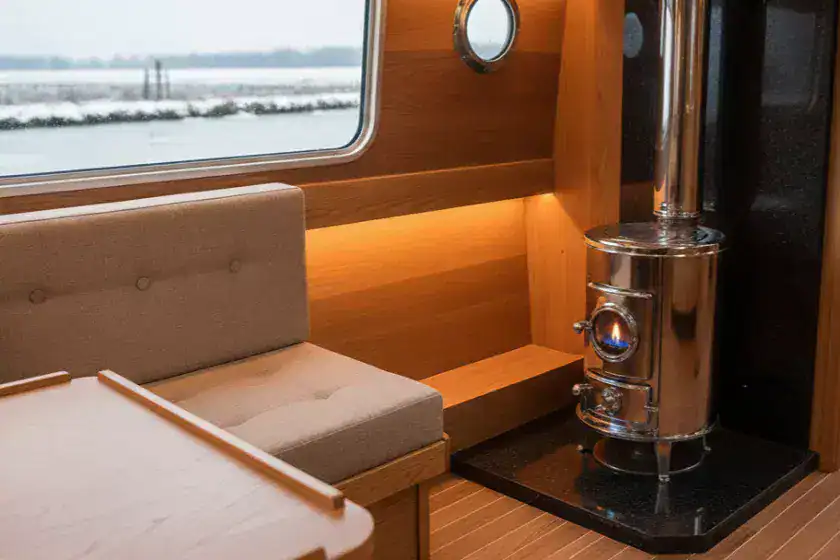 A clean, stainless steel Refleks diesel stove installed in a narrowboat corner. The stove shows a steady blue flame through the sight glass with no smoke or wood present, representing a clean-burning marine heating system.