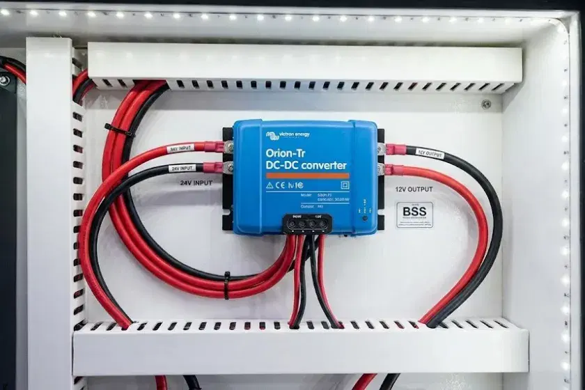 A professional photo of a Victron Orion-Tr 24 to 12V DC-DC converter mounted on a fire-resistant bulkhead in a boat’s engine room, showing neatly labeled input and output wiring.