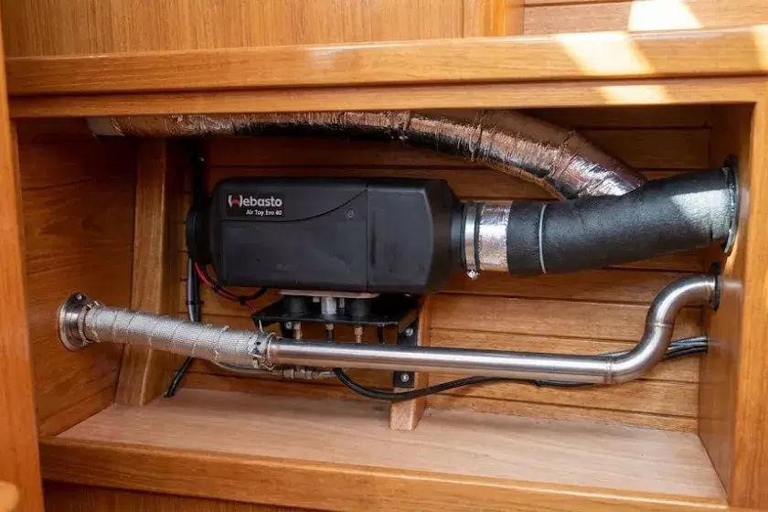 A high-resolution photograph of a Webasto Air Top Evo 40 diesel heater professionally installed in a boat's timber-lined locker, showing clean ducting, a secured fuel line, and a double-insulated marine exhaust.