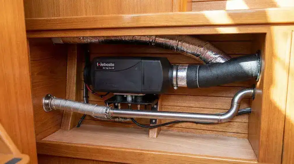 A high-resolution photograph of a Webasto Air Top Evo 40 diesel heater professionally installed in a boat's timber-lined locker, showing clean ducting, a secured fuel line, and a double-insulated marine exhaust.