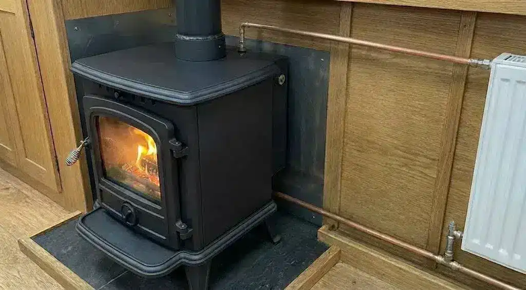 A professionally installed canal boat central heating system featuring a clean cast iron back boiler stove connected by neat copper pipework to a modern white radiator.