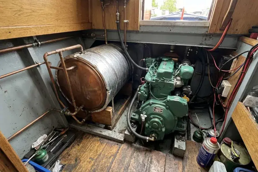 A typical narrowboat calorifier installation featuring a vertical copper-colored insulated tank, marine-grade rubber hoses, and secure mounting within a traditional engine compartment.