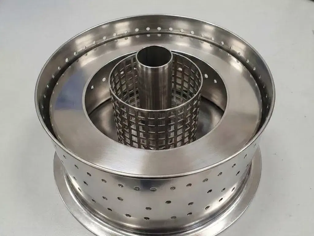 A close-up view of a clean Refleks diesel heater burner pot on a metal workbench, showing the perforated stainless steel construction and central vaporising tube.