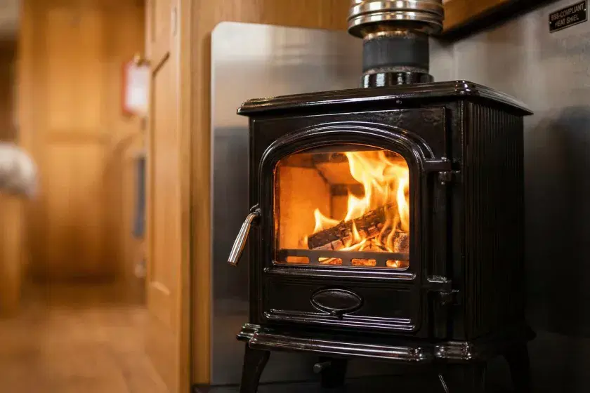 A professionally installed solid fuel boat stove with a fire-lit chamber, twin-wall insulated flue, and BSS-compliant heat shielding in a narrowboat interior.