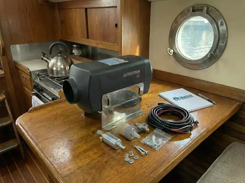 A new Autoterm 4D diesel heater unit sitting on a wooden galley table next to a Marine Heating Solutions branded notepad.
