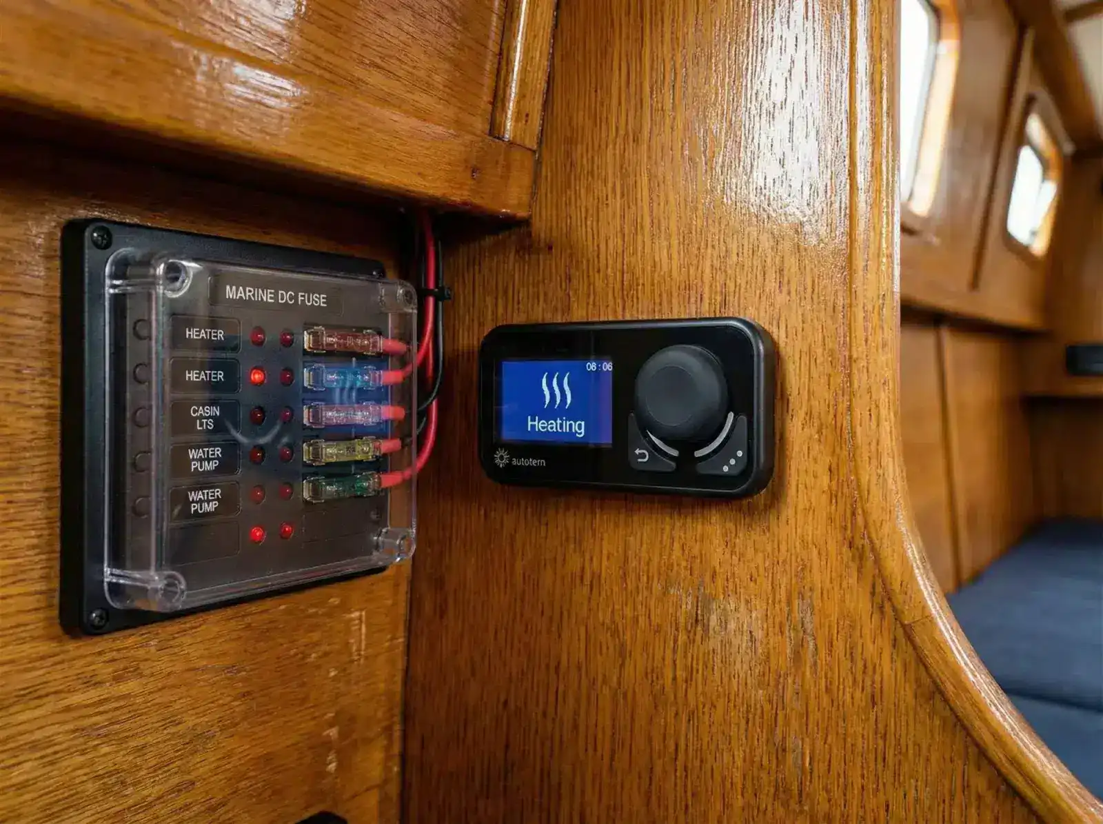 A close-up of an Autoterm Comfort Control thermostat mounted on a wooden bulkhead next to a marine fuse panel and 12V switches.

