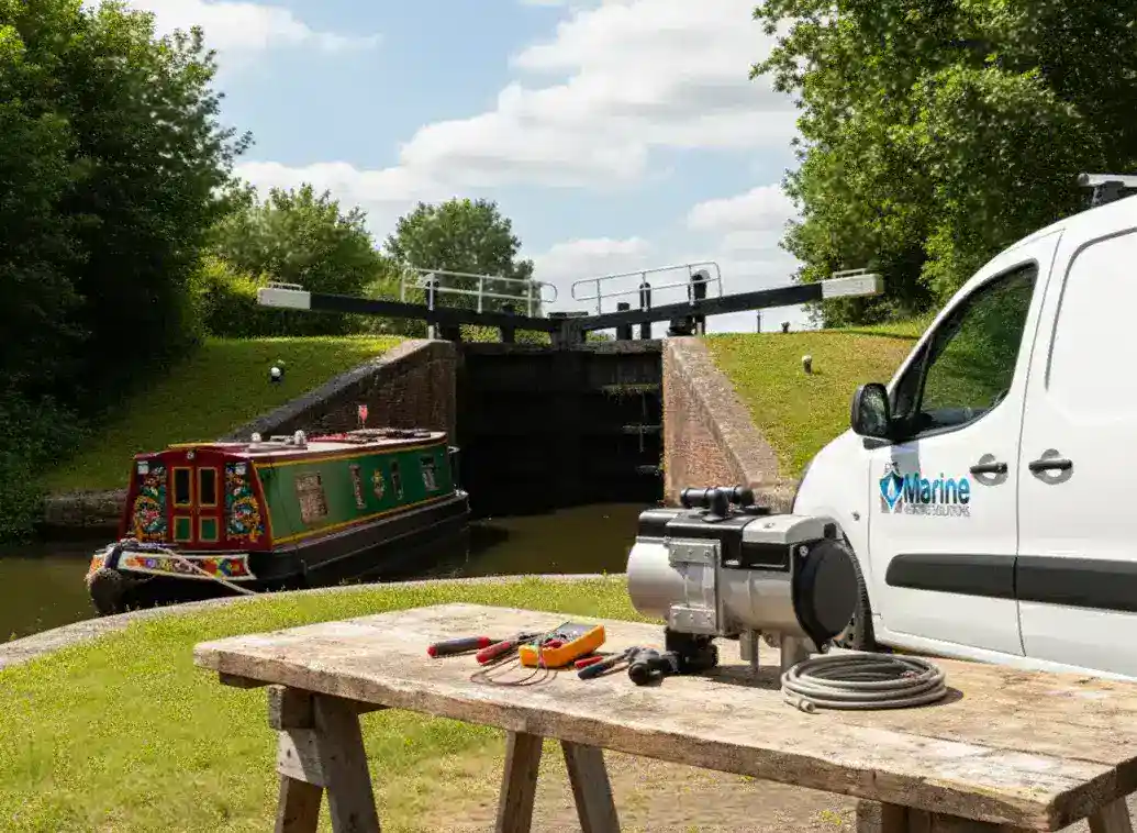 An Autoterm Flow 5 liquid heater on a wooden workbench next to a Marine Heating Solutions van, with a traditional narrowboat exiting a canal lock in the background.
