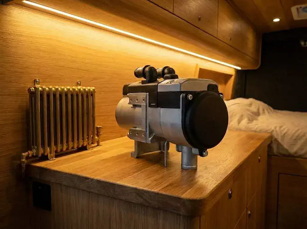 Autoterm Flow 5 diesel liquid heater unit with top-mounted hose tails, shown as a bare unit in a wooden boat interior.