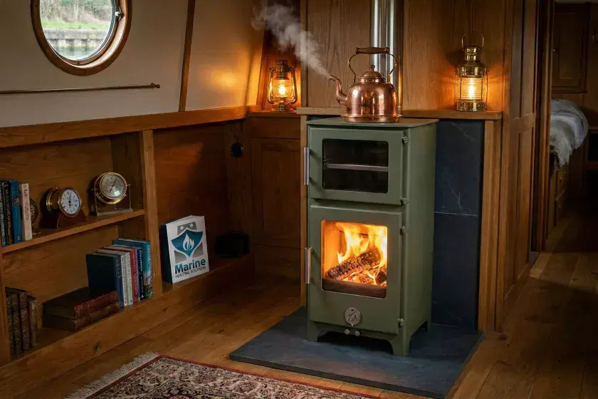 A professional installation of a Chilli Penguin Tall Hungry Penguin multifuel boat stove in Evergreen, featuring a traditional copper kettle on the hotplate and a realistic wood fire inside a narrowboat cabin.