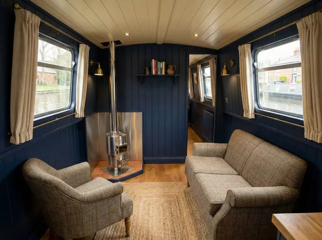 Installation of a Dickinson Antarctic diesel stove in a blue-walled narrowboat lounge featuring a grey sofa and armchair.