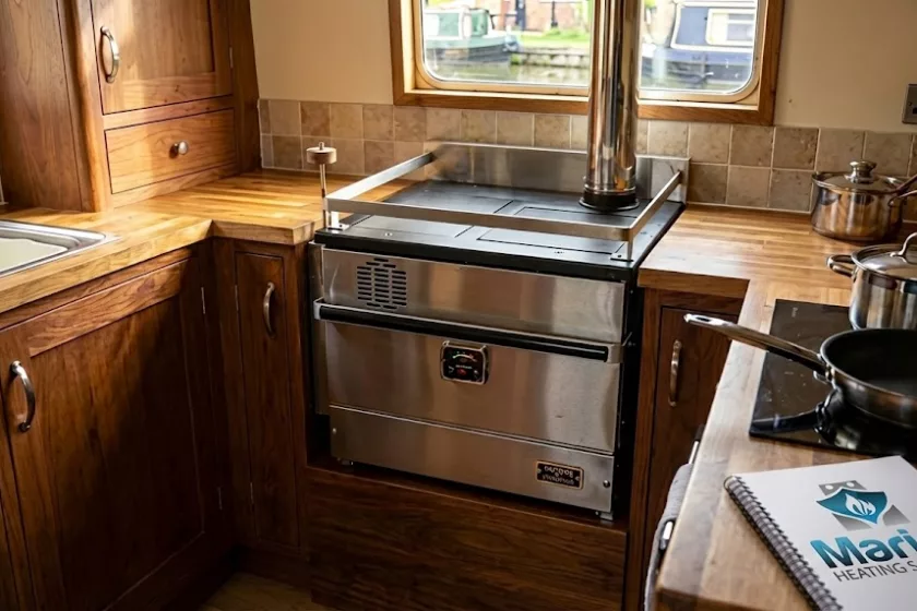 A stainless steel Dickinson Bristol diesel cooker installed on a wooden plinth in a narrowboat galley with a vertical flue and wooden worktops.