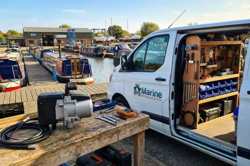 An Eberspacher Hydronic S3 D5 marine diesel heater on a workbench next to a branded Marine Heating Solutions service van at a narrowboat marina.