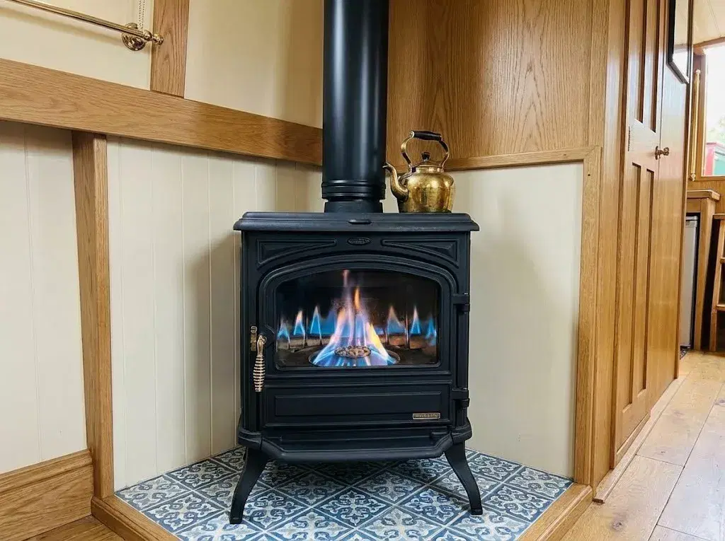 Close-up of a Franco Belge Burgundy 10kW oil stove showing the blue flame through the large glass window, installed with a black insulated flue in a boat cabin.