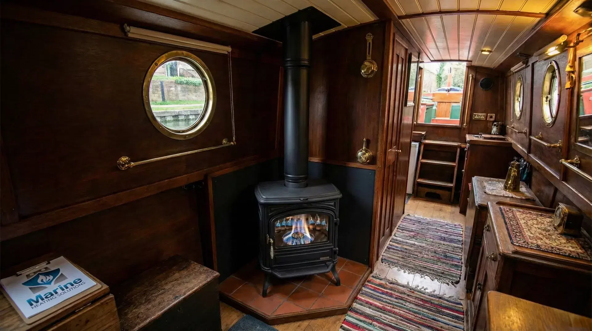 A 10kW Franco Belge Burgundy oil stove with a black twin-wall insulated flue installed in a wood-paneled narrowboat cabin, featuring a Marine Heating Solutions clipboard.