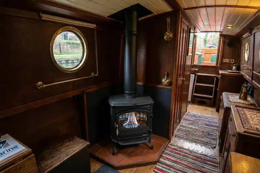 A 10kW Franco Belge Burgundy oil stove with a black twin-wall insulated flue installed in a wood-paneled narrowboat cabin, featuring a Marine Heating Solutions clipboard.