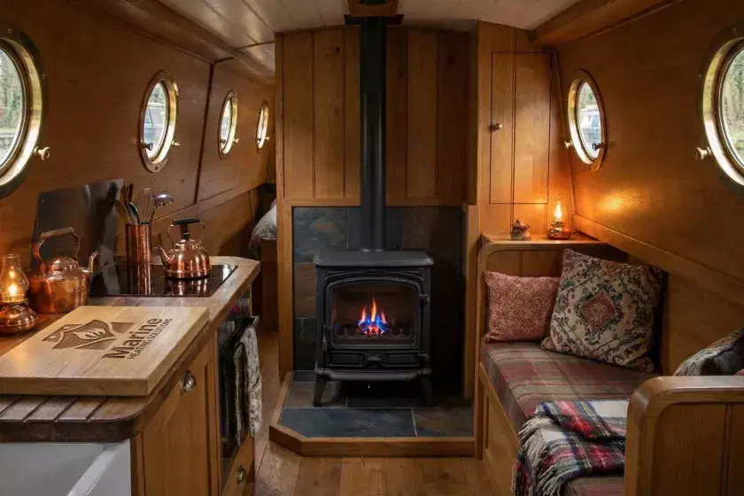 A Franco Belge Savoy oil-burning stove installed in a cozy narrowboat galley with a branded Marine Heating Solutions wooden chopping board on the worktop.