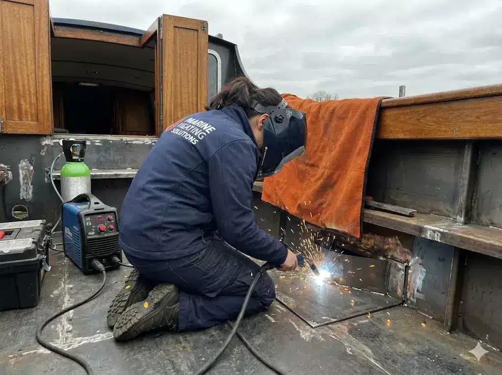 A female marine engineer welding a steel boat hull using professional mobile equipment and a fire safety blanket.
