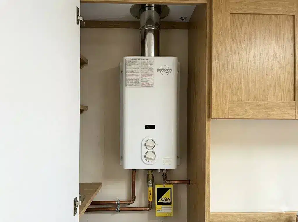 A professional GasSafe registered installation of a Morco D61B LPG water heater inside a narrowboat cupboard, featuring BSS-compliant pipework routed through the cabinetry and a correctly fitted flue system.