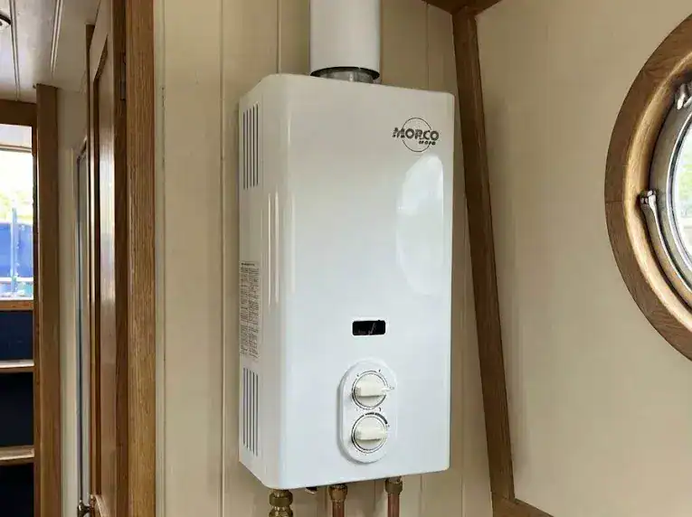 A professional GasSafe-compliant installation of a Morco D61B LPG water heater on a narrowboat bulkhead, featuring a white vertical flue and a central gas isolation valve.