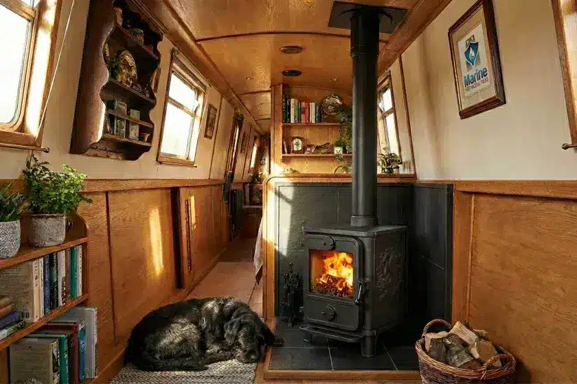 A traditional cast-iron Morso wood burning stove with a black twin-wall insulated flue installed in a wood-paneled narrowboat.