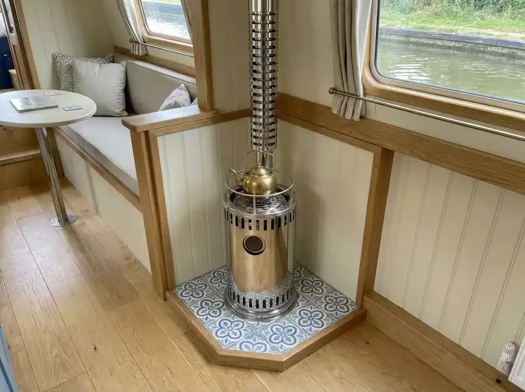 A Refleks 61M diesel stove with a polished finish installed in a modern narrowboat cabin, featuring light wood walls and a sleek slate hearth.