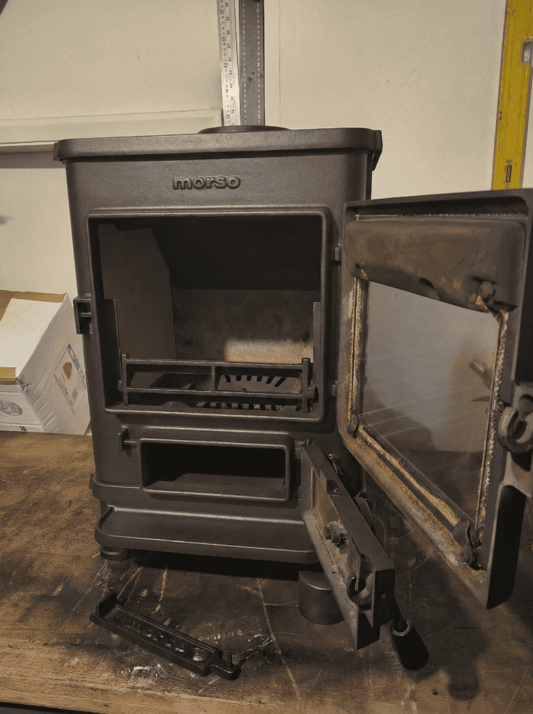 A refurbished Morso Squirrel boat stove on a workbench, with its doors open. A clean interior with new firw bricks can be seen.