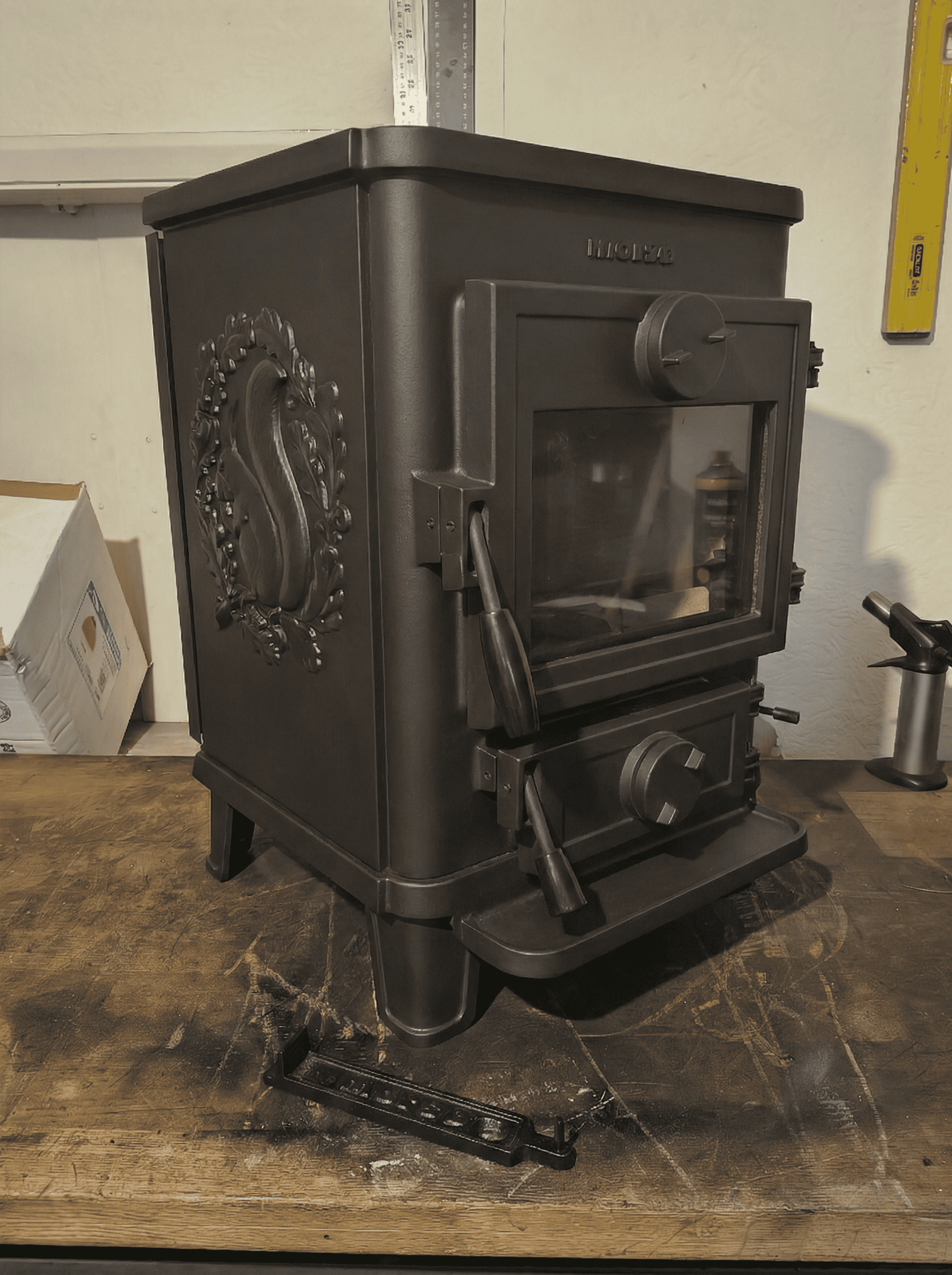 A refurbished Morso Squirrel 1412 Stove, sittting on  a workbench, showing front and right hand side panel with squirrel motif.