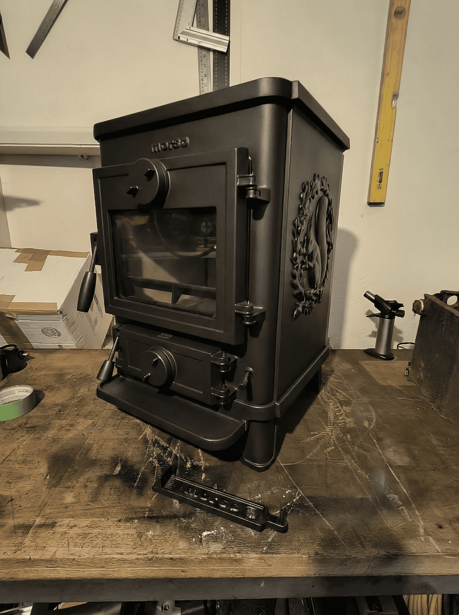 A refurbished Morso Squirrel 1412 Stove, sittting on  a workbench, showing front and right hand side panel with squirrel motif.