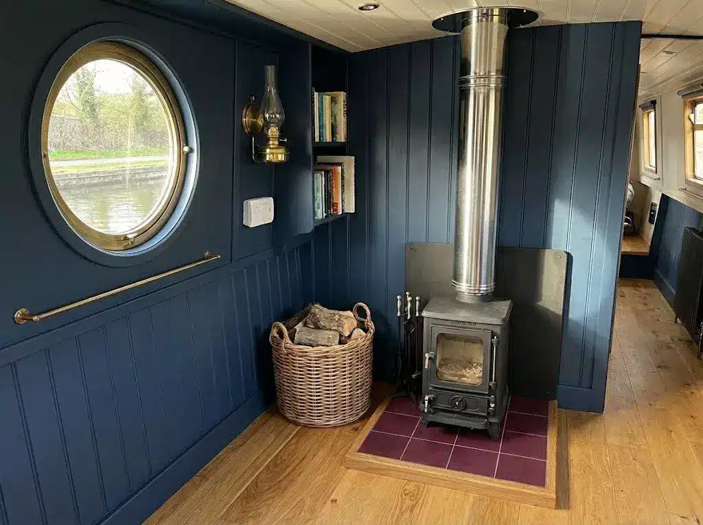 A professional BSS-compliant installation of a Salamander Hobbit multi-fuel stove kit in a narrowboat saloon, featuring a raised tiled hearth, a twin-wall insulated flue, and a wall-mounted Carbon Monoxide alarm.