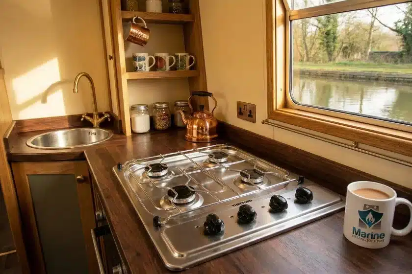 Thetford 8 Series 4-burner stainless steel LPG hob installed in a narrowboat kitchen next to a Marine Heating Solutions branded mug.