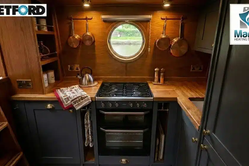Thetford Cocina black glass LPG cooker installed in a modern narrowboat galley with wood interiors and a porthole window.