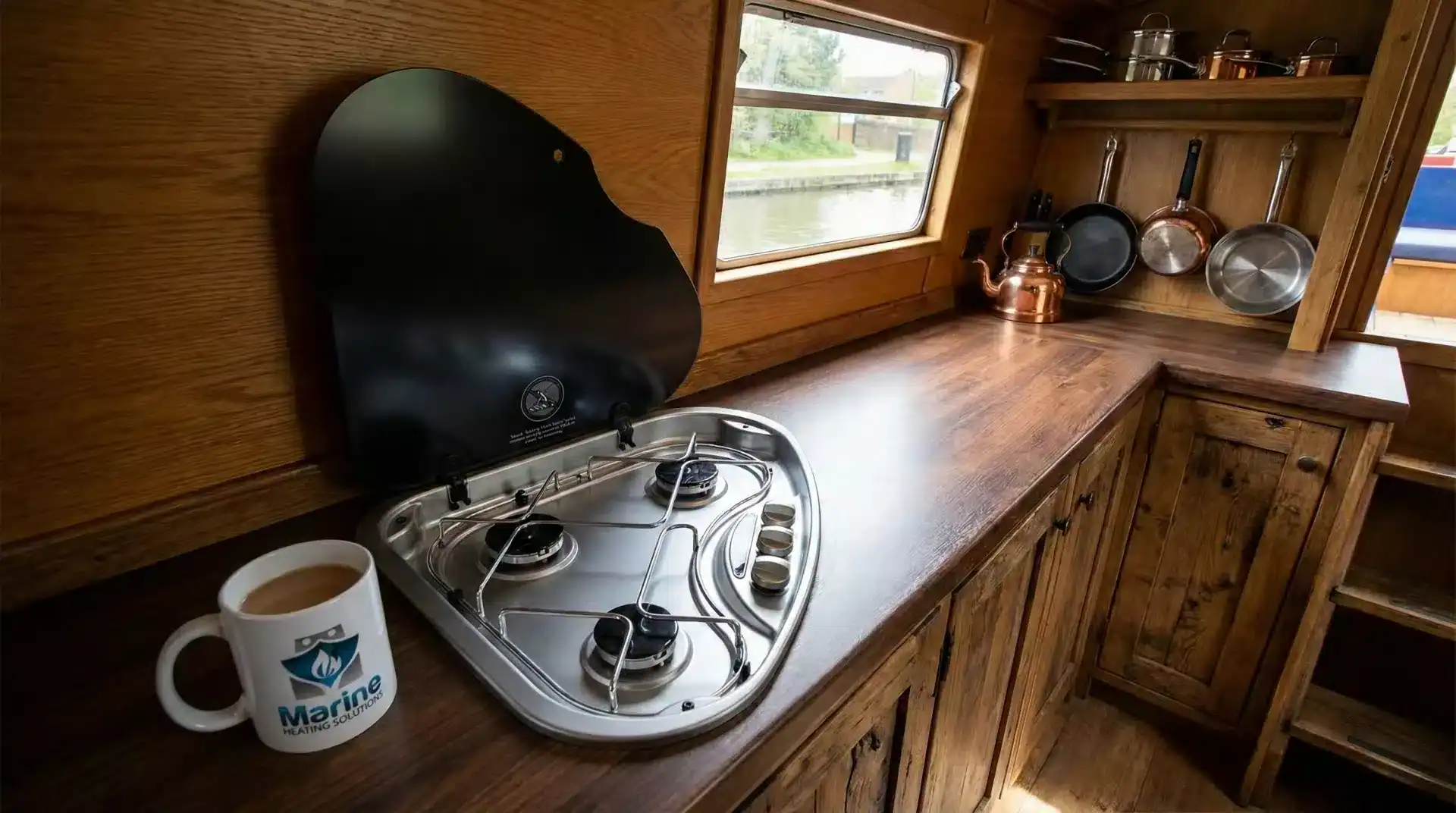 Thetford Series 330 triangular 3-burner LPG gas hob installed in a wooden narrowboat kitchen galley next to a Marine Heating Solutions branded mug.