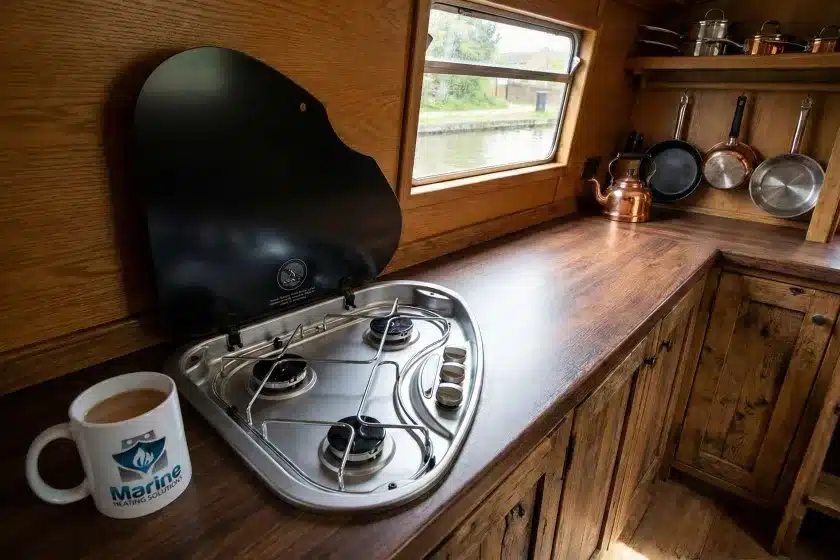 Thetford Series 330 triangular 3-burner LPG gas hob installed in a wooden narrowboat kitchen galley next to a Marine Heating Solutions branded mug.