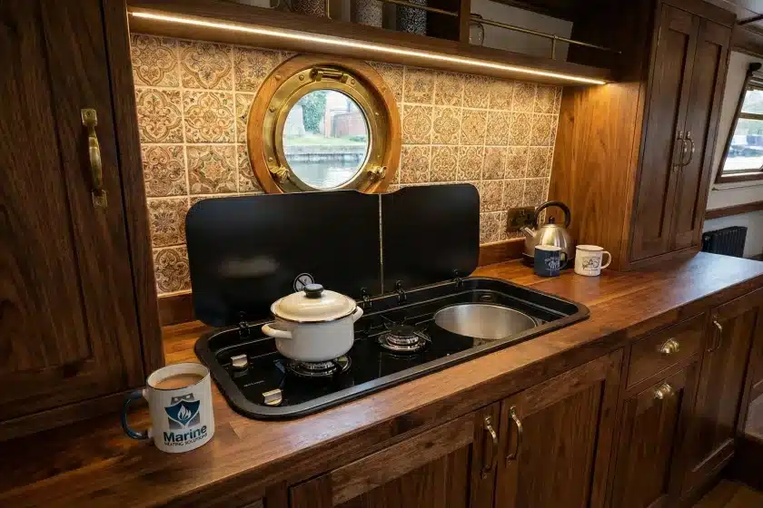 Thetford Topline 111 LPG hob and sink combination unit with black glass lid installed in a rustic narrowboat kitchen with wooden cabinetry and decorative tiles.